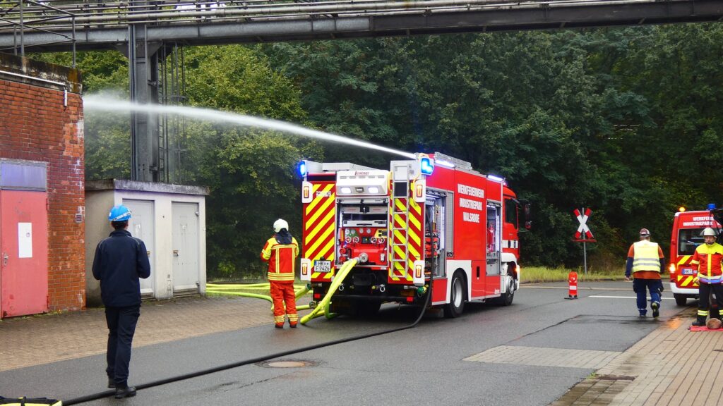 Feuerwehr löscht Brand mit Löschschlauch bei Industriegebäude.