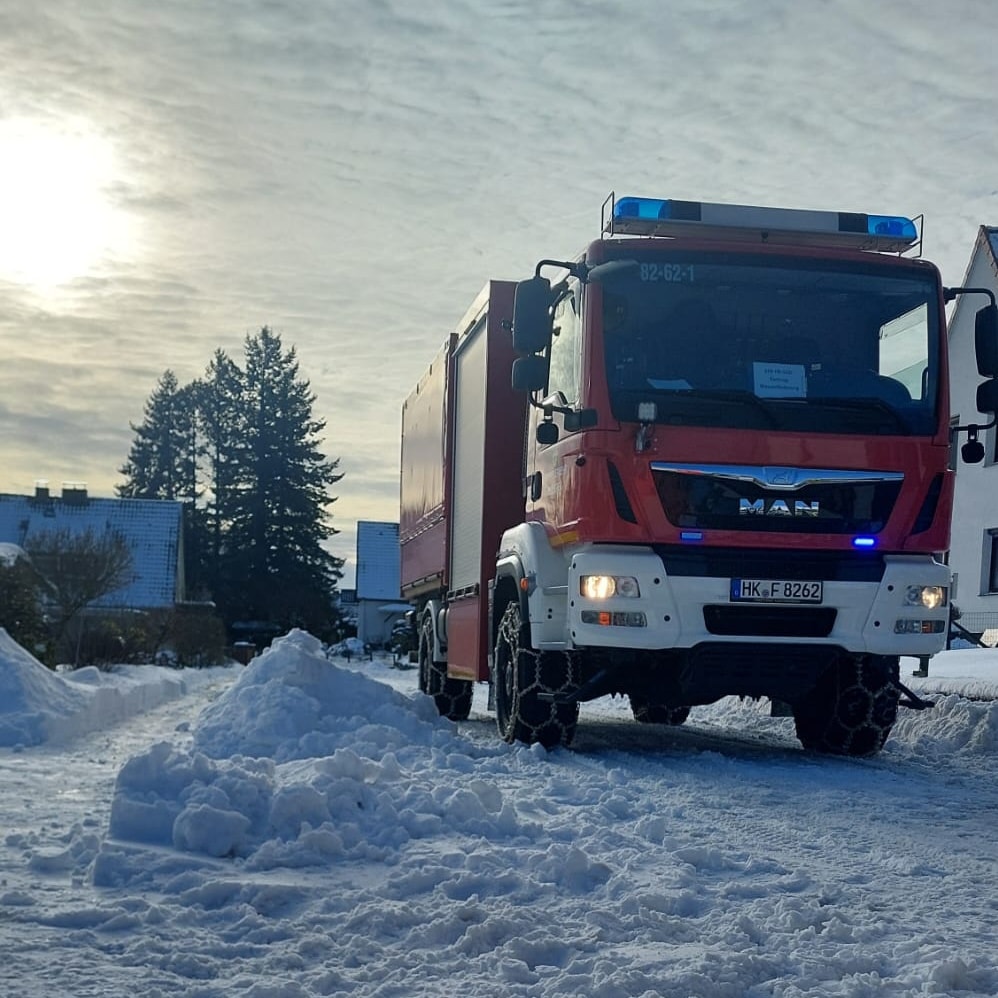 Feuerwehrfahrzeug fährt auf schneebedeckter Straße.