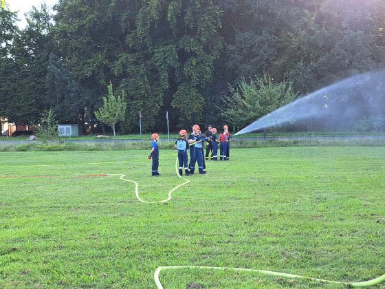Jugendfeuerwehr übt mit Wasserschlauch auf Wiese.